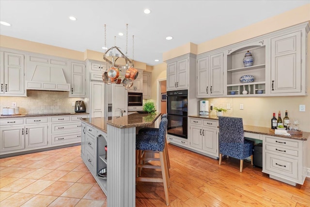 kitchen with a kitchen bar, dark stone counters, black appliances, white cabinetry, and an island with sink