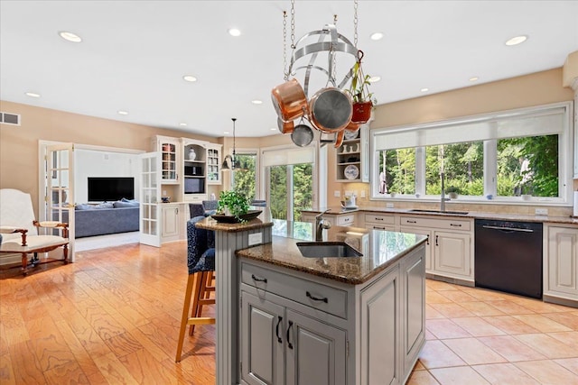 kitchen featuring a kitchen island with sink, sink, dark stone countertops, black dishwasher, and gray cabinets