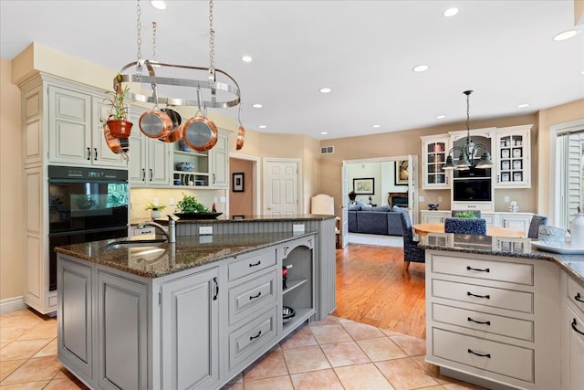 kitchen featuring dark stone counters, a kitchen island with sink, sink, light tile patterned floors, and hanging light fixtures