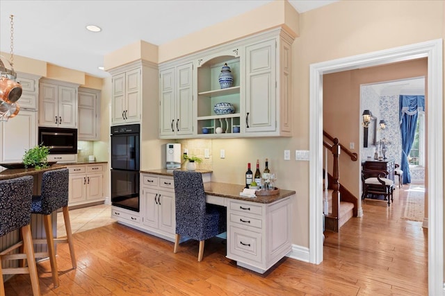 kitchen with black double oven, decorative backsplash, built in microwave, light hardwood / wood-style floors, and a kitchen bar