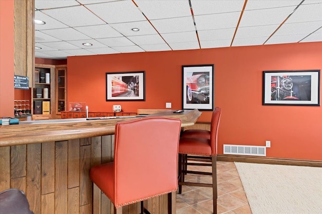 bar with light tile patterned floors and a drop ceiling