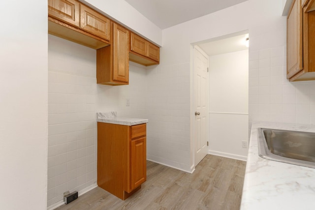 kitchen with light stone countertops, sink, tile walls, and light wood-type flooring