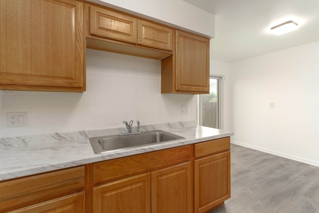 kitchen featuring light stone countertops, backsplash, light hardwood / wood-style flooring, and sink