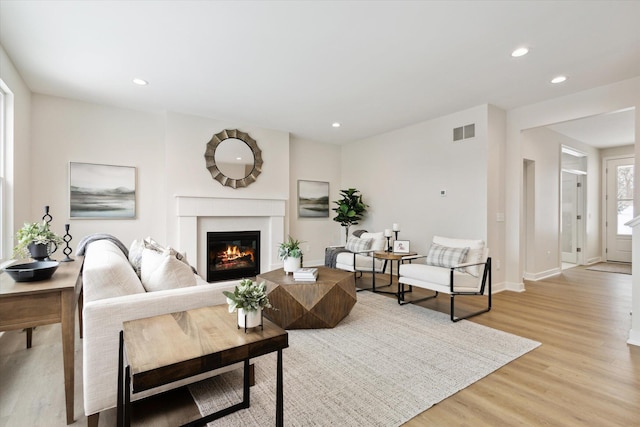 living area with recessed lighting, visible vents, a glass covered fireplace, light wood-type flooring, and baseboards