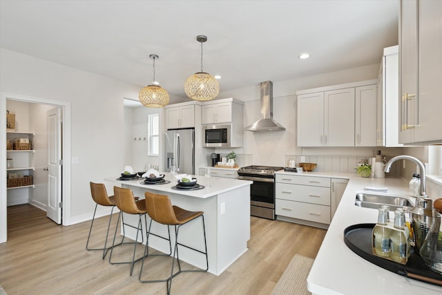 kitchen featuring wall chimney exhaust hood, a kitchen island, stainless steel appliances, white cabinetry, and a sink