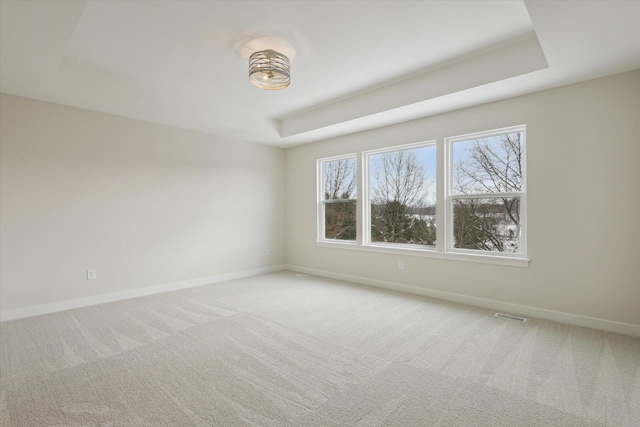 carpeted spare room featuring a raised ceiling, visible vents, and baseboards