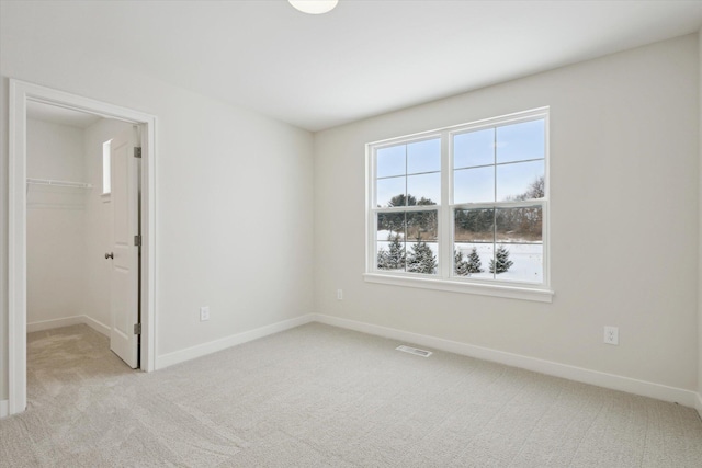 unfurnished bedroom with light carpet, a spacious closet, visible vents, and baseboards