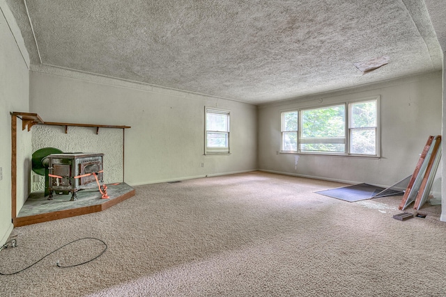 unfurnished living room featuring a wood stove, carpet floors, and a textured ceiling