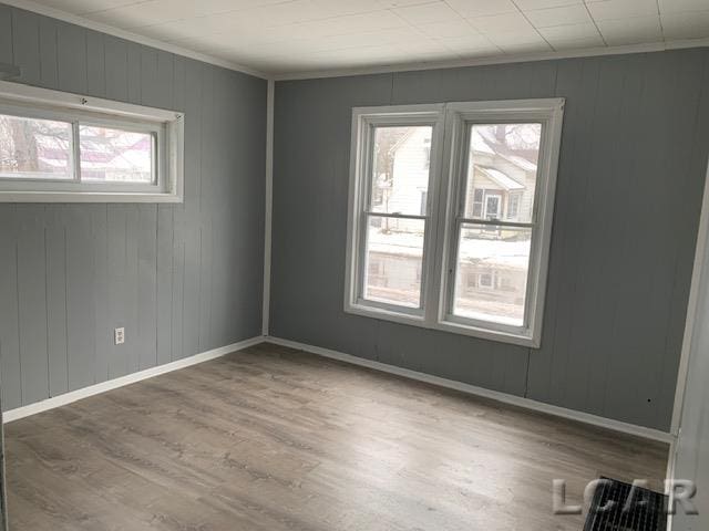 empty room with wood walls, a healthy amount of sunlight, wood-type flooring, and crown molding