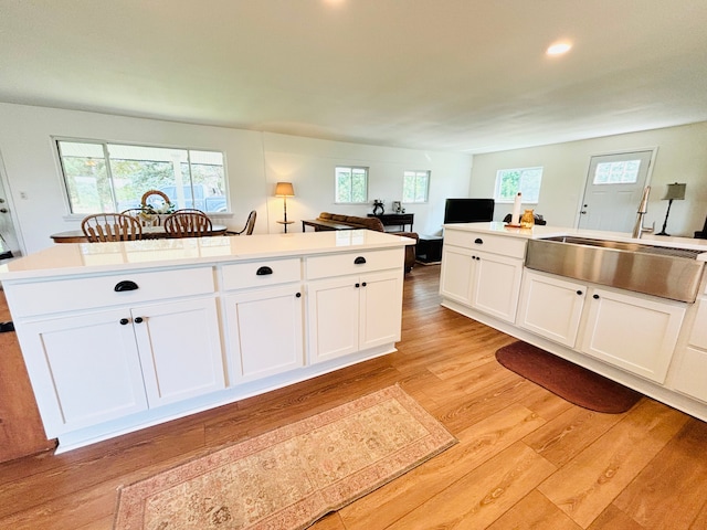 kitchen with white cabinetry, light hardwood / wood-style flooring, a kitchen island, and sink