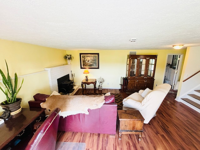 living room featuring dark wood-type flooring, a textured ceiling, and a brick fireplace