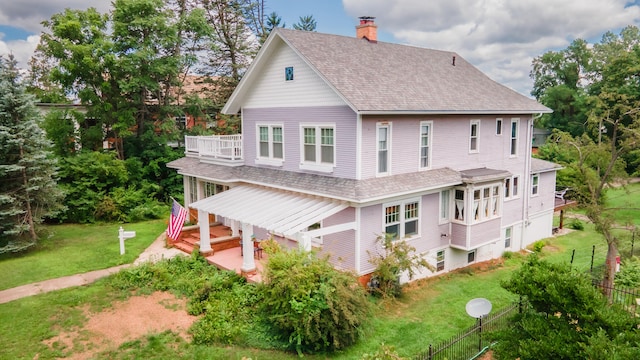 rear view of property with a balcony and a lawn