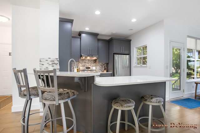 kitchen with backsplash, stainless steel fridge, light hardwood / wood-style floors, a breakfast bar area, and a kitchen island