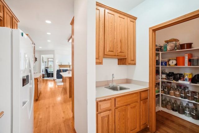 kitchen with a sink, light countertops, white fridge with ice dispenser, recessed lighting, and light wood-type flooring