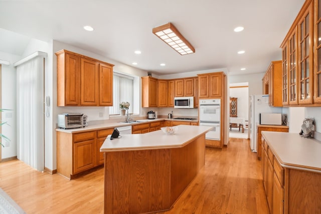 kitchen featuring a kitchen island, white appliances, light countertops, a sink, and light wood finished floors