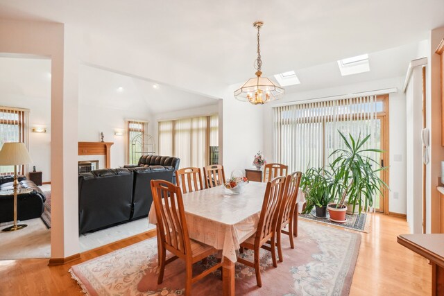 dining room with light wood-style floors, lofted ceiling with skylight, a chandelier, and a fireplace