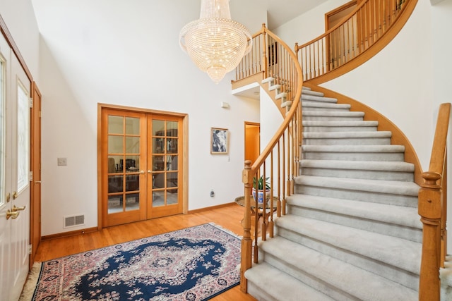 staircase featuring an inviting chandelier, french doors, baseboards, a towering ceiling, and visible vents