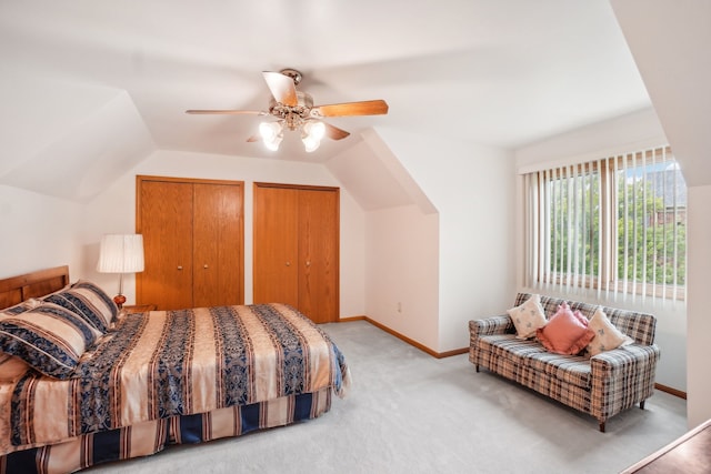bedroom featuring ceiling fan, light colored carpet, vaulted ceiling, baseboards, and two closets