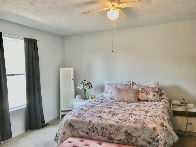 bedroom featuring multiple windows, light carpet, a textured ceiling, and ceiling fan