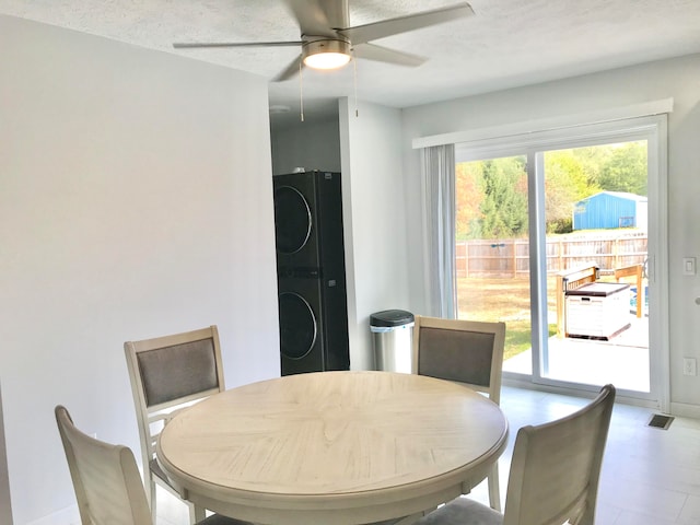 dining space featuring ceiling fan, stacked washing maching and dryer, and a textured ceiling