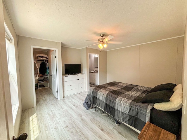 bedroom with ensuite bathroom, a walk in closet, ceiling fan, light hardwood / wood-style floors, and a closet