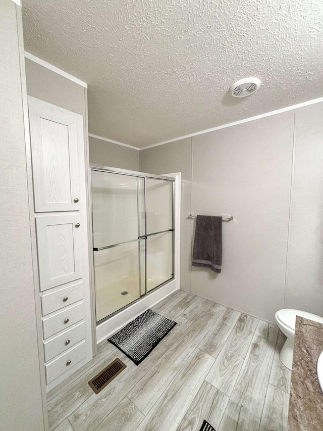 bathroom featuring toilet, wood-type flooring, a textured ceiling, and walk in shower