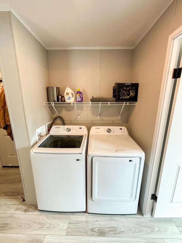 clothes washing area featuring crown molding, washer and dryer, and light hardwood / wood-style floors