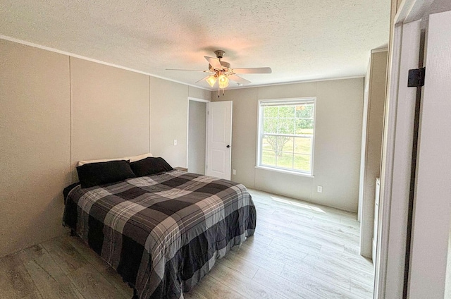 bedroom with ceiling fan, light hardwood / wood-style floors, ornamental molding, and a textured ceiling