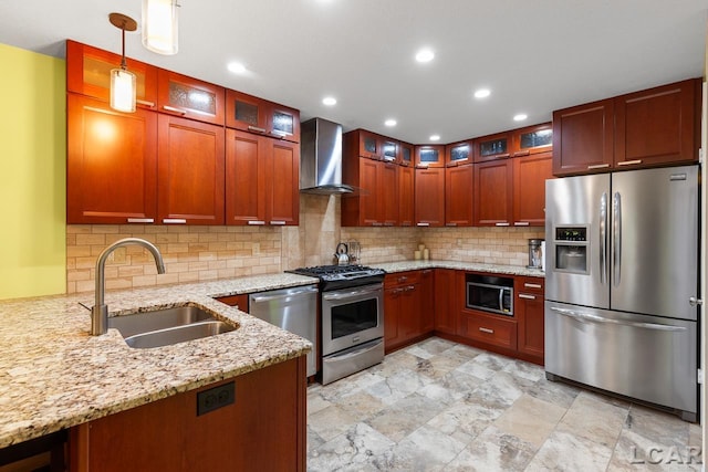 kitchen with light stone countertops, wall chimney exhaust hood, stainless steel appliances, sink, and hanging light fixtures