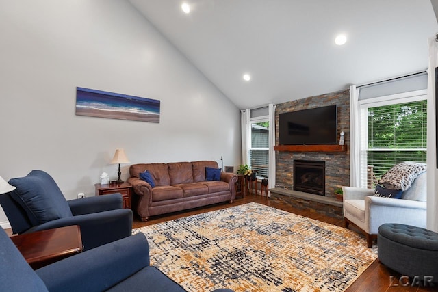 living room with dark hardwood / wood-style flooring, high vaulted ceiling, a stone fireplace, and a wealth of natural light