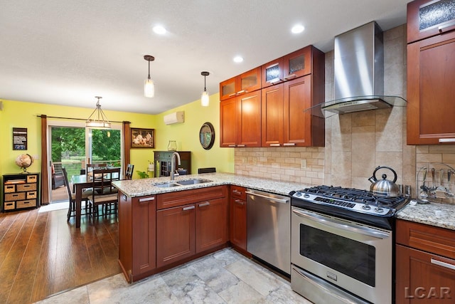 kitchen with hanging light fixtures, sink, wall chimney exhaust hood, appliances with stainless steel finishes, and kitchen peninsula