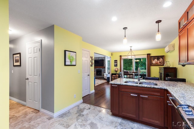 kitchen with light stone counters, sink, light hardwood / wood-style flooring, an AC wall unit, and hanging light fixtures