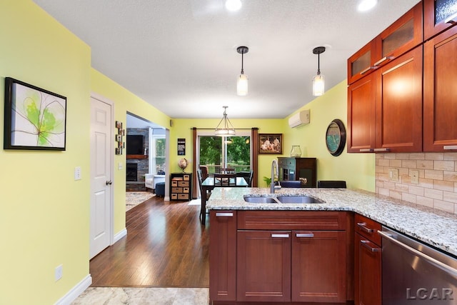 kitchen with dark wood-type flooring, an AC wall unit, sink, stainless steel dishwasher, and light stone countertops