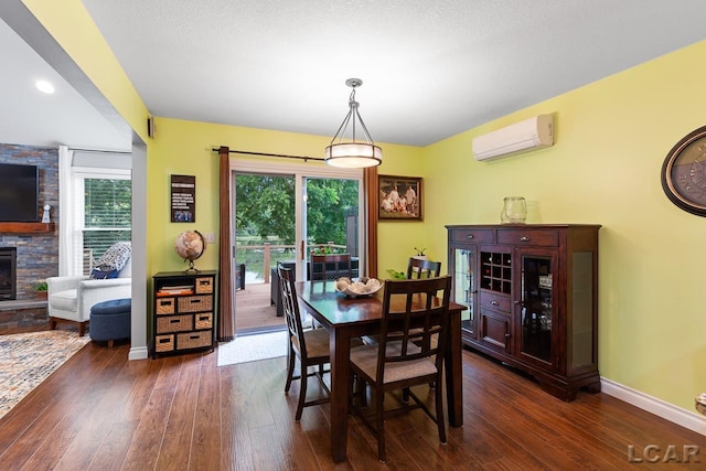 dining room featuring a healthy amount of sunlight, a stone fireplace, an AC wall unit, and dark wood-type flooring