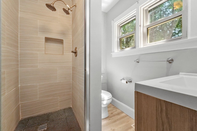 bathroom featuring hardwood / wood-style flooring, vanity, toilet, and a tile shower