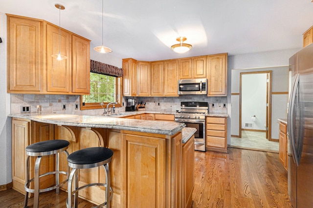 kitchen with kitchen peninsula, backsplash, stainless steel appliances, light hardwood / wood-style floors, and hanging light fixtures