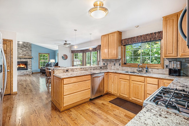 kitchen featuring sink, a stone fireplace, pendant lighting, appliances with stainless steel finishes, and light wood-type flooring