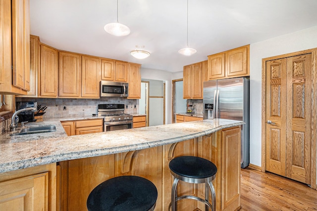 kitchen featuring kitchen peninsula, appliances with stainless steel finishes, tasteful backsplash, pendant lighting, and light hardwood / wood-style flooring