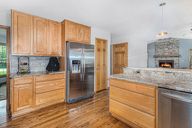 kitchen featuring light stone countertops, appliances with stainless steel finishes, pendant lighting, dark hardwood / wood-style floors, and a stone fireplace