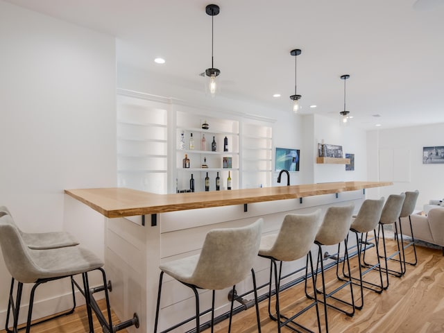 bar with wood counters, light wood-type flooring, hanging light fixtures, and sink