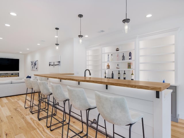 bar featuring wood counters, light hardwood / wood-style flooring, hanging light fixtures, and built in features