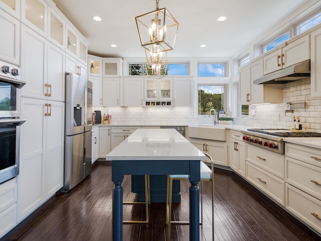 kitchen with sink, dark wood-type flooring, backsplash, decorative light fixtures, and appliances with stainless steel finishes