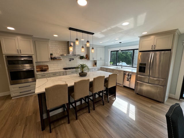 kitchen featuring stainless steel appliances, decorative backsplash, wall chimney range hood, a kitchen island, and light stone counters