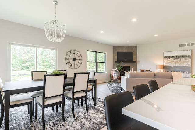 dining area with plenty of natural light, wood-type flooring, a tile fireplace, and an inviting chandelier