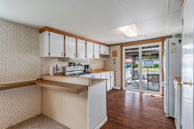 kitchen with dark wood-type flooring, kitchen peninsula, white appliances, a paneled ceiling, and white cabinets