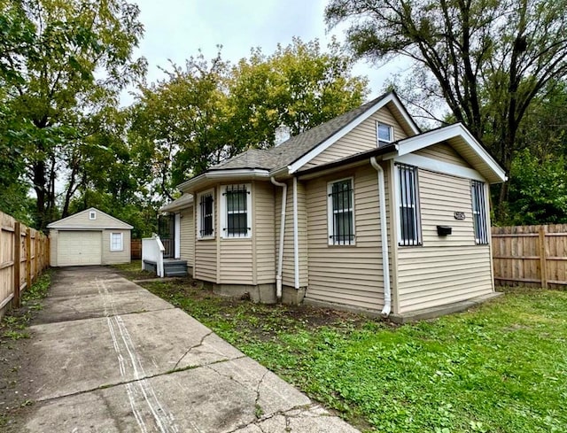 view of front of house featuring a detached garage, fence, concrete driveway, a front yard, and an outbuilding