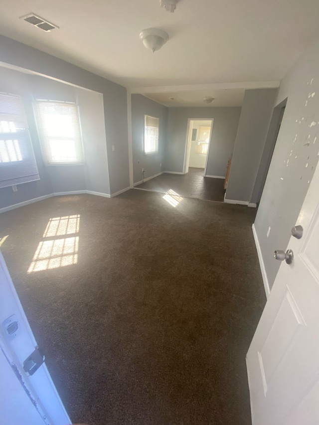 spare room with visible vents, a healthy amount of sunlight, baseboards, and dark carpet