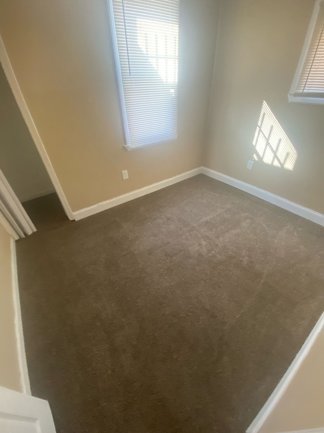 spare room featuring baseboards and dark colored carpet