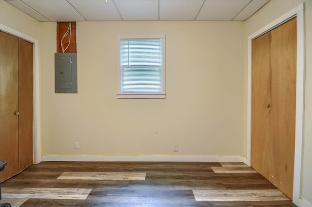 unfurnished bedroom with dark wood-type flooring, a paneled ceiling, electric panel, and a closet