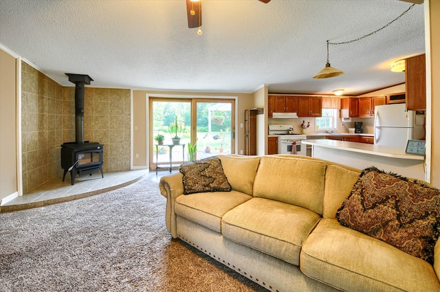 carpeted living room with ceiling fan, lofted ceiling, a textured ceiling, and a wood stove